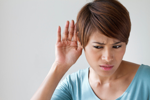 Woman holds a hand to her ear, struggling to hear due to noise-induced hearing loss.
