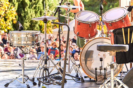 Drumset on a stage at an outdoor music festival. The crowd is full and expectant.