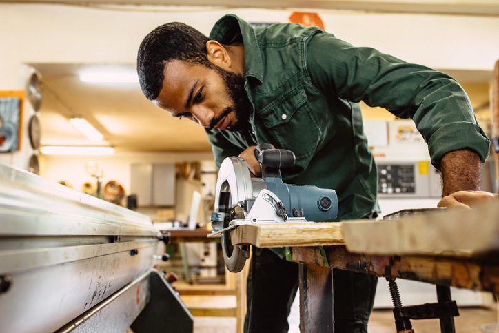 Man leaning over piece of wood using circular saw to cut it in his home workshop